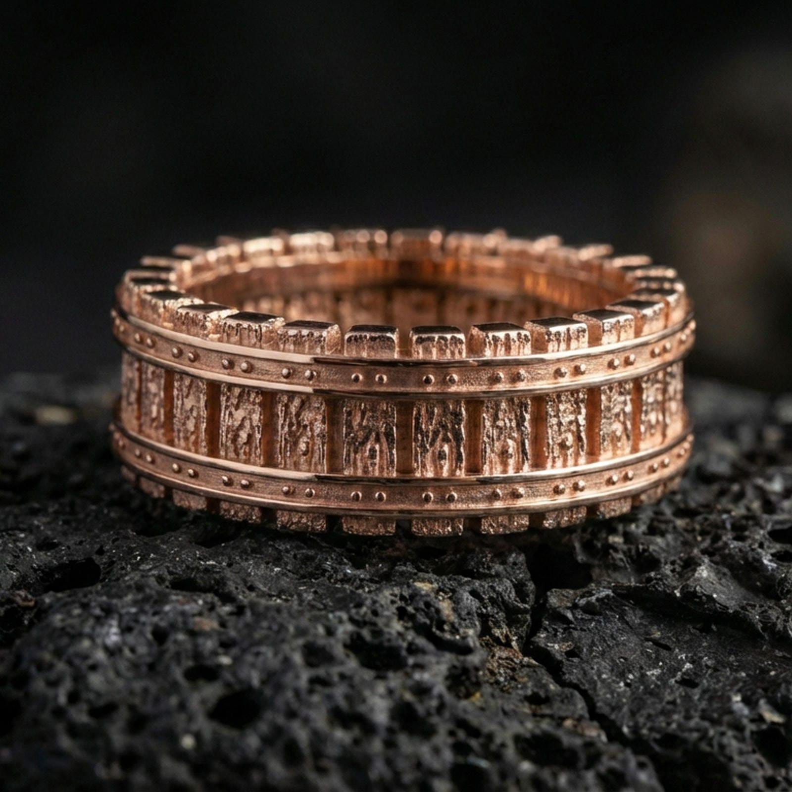 Rose gold plated sterling silver machinist railway band on volcanic stone, industrial track texture with bold rivet accents, minimal high-end close-up.