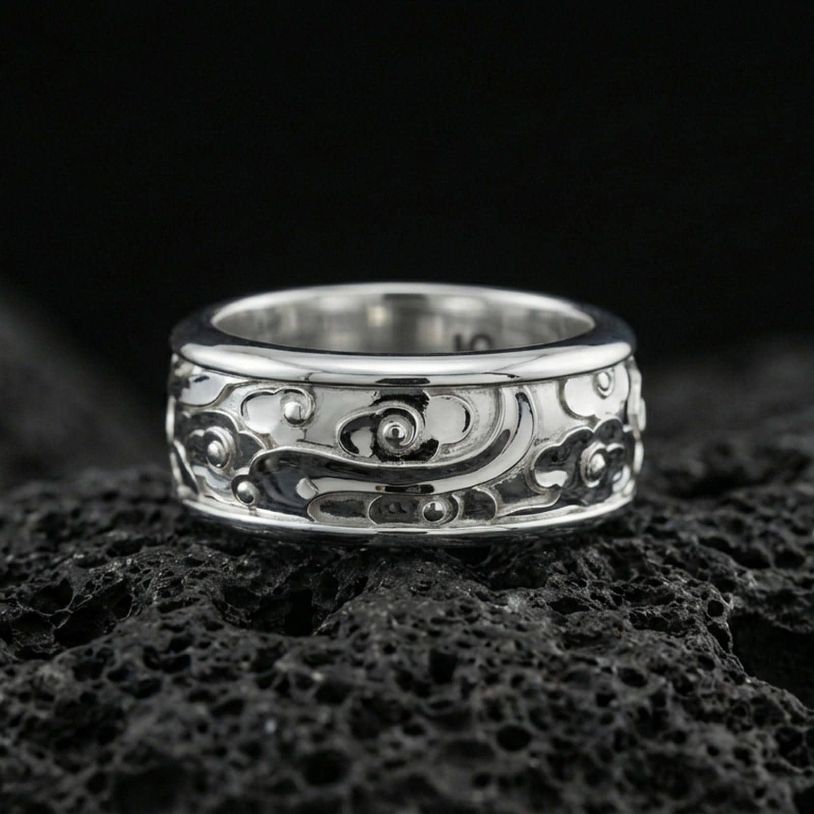 Polished silver fidget spinner cloud and flower band ring on black volcanic stone, crisp cartoon-style swirl relief with smooth comfort edges, centered close-up studio lighting.