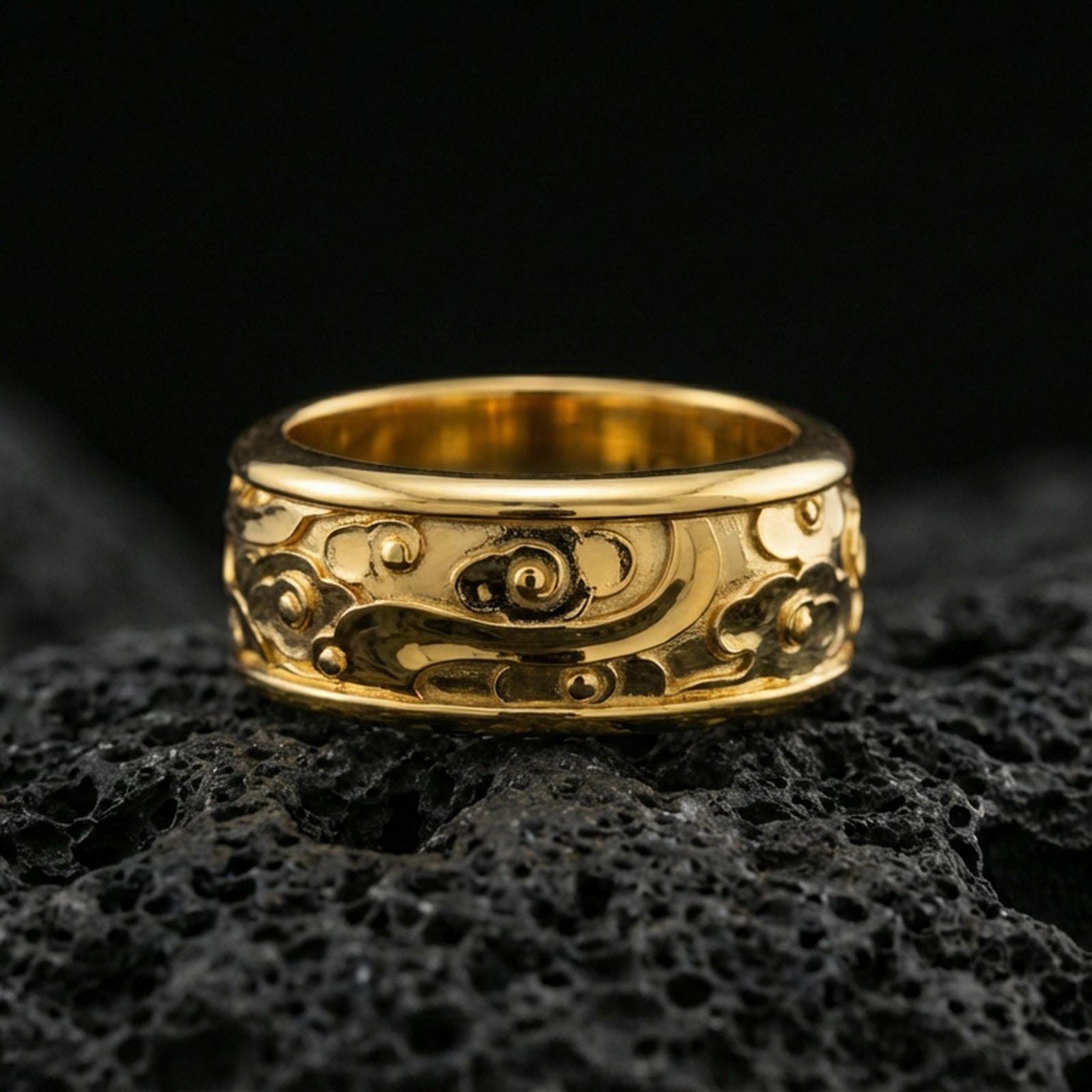 Gold plated spinning cloud motif band ring on volcanic rock, detailed swirl and floral relief on rotating band, luxury jewelry product photography.