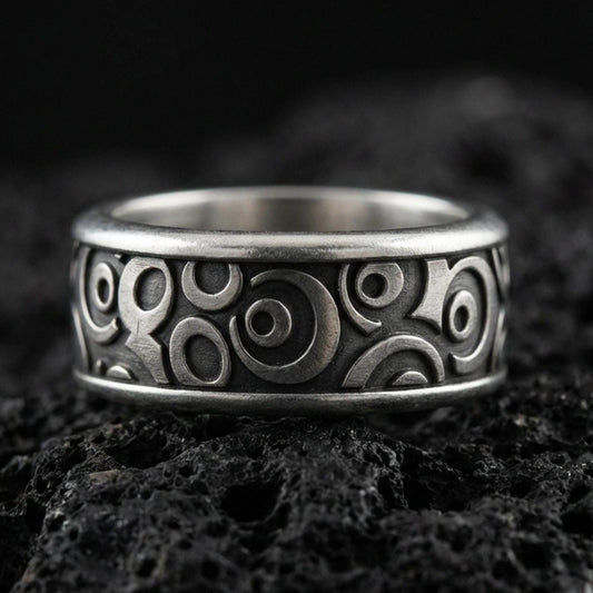 Oxidized sterling silver geometric spinner band ring on dark volcanic rock, raised circular pattern on rotating center, premium macro product shot.