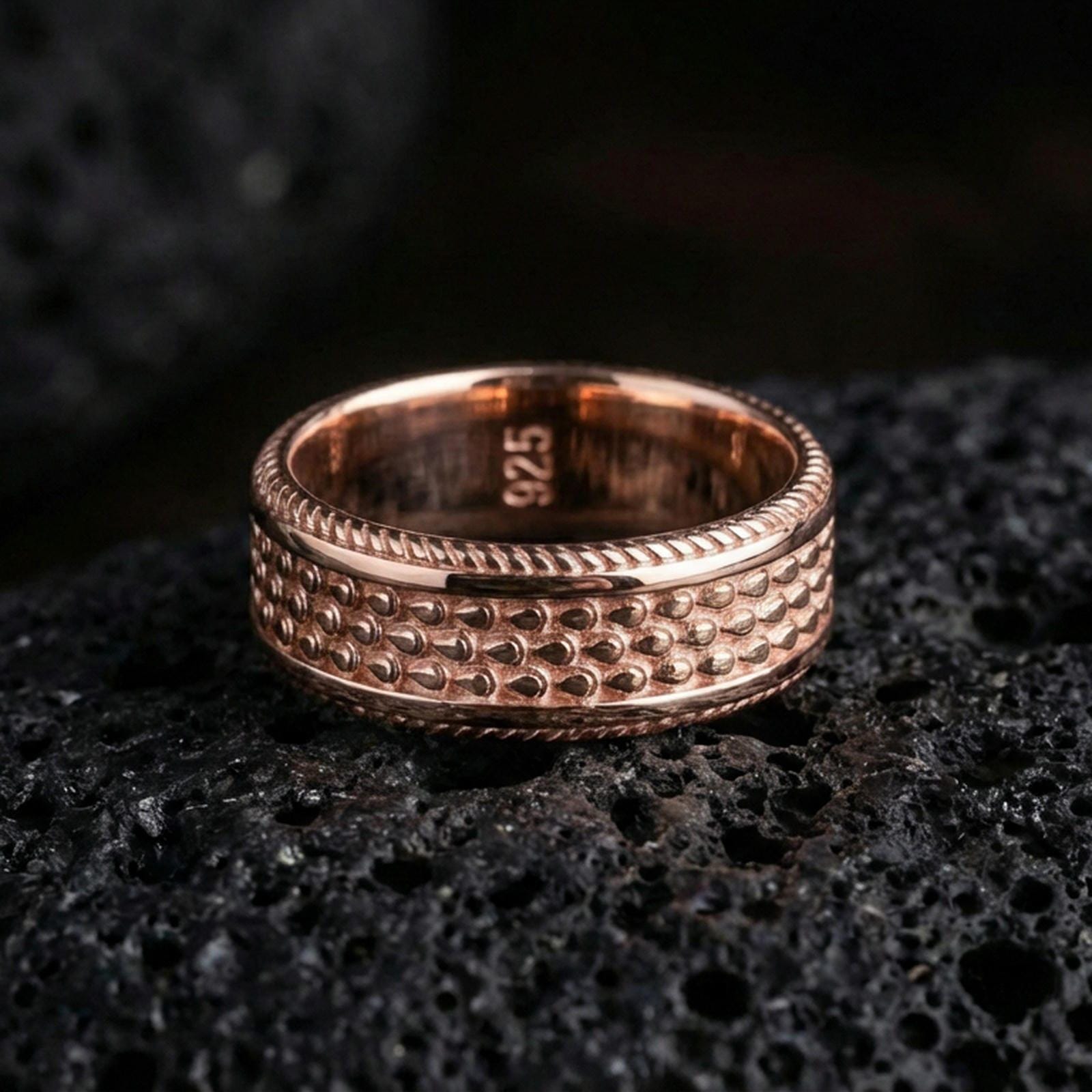 Rose gold plated sterling silver beaded texture band on volcanic stone, raised dot pattern with deep contrast and ridged edges, minimal high-end close-up.