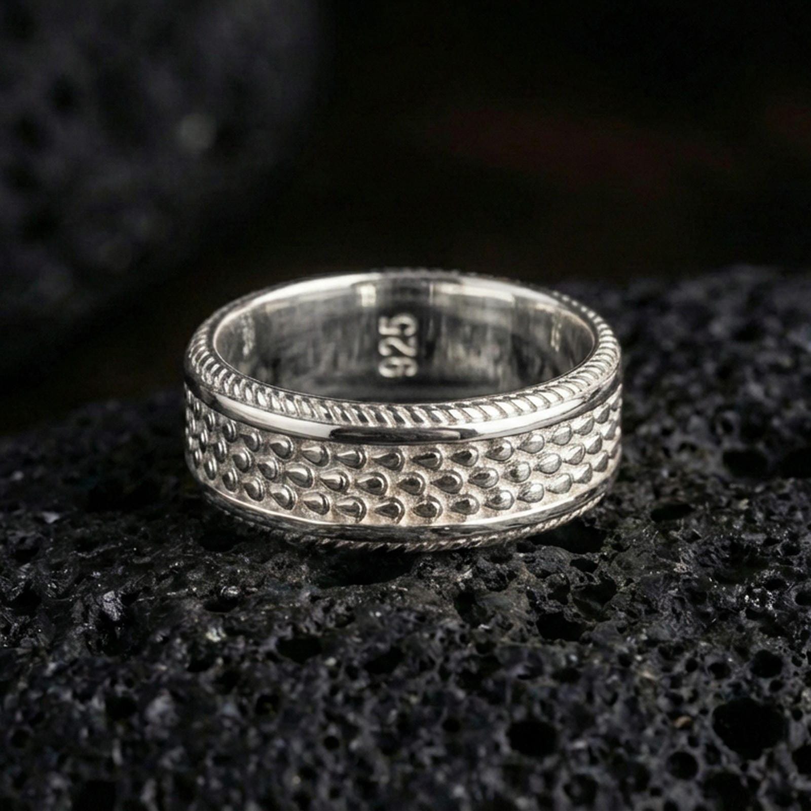 Polished silver dot texture band ring on black volcanic stone, crisp beaded pattern detail and ridged edge accents, centered close-up studio lighting.