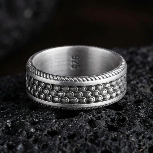 Oxidized sterling silver beaded dot texture band ring on dark volcanic rock, hammered bubble pattern with rope edge border, premium macro product shot.