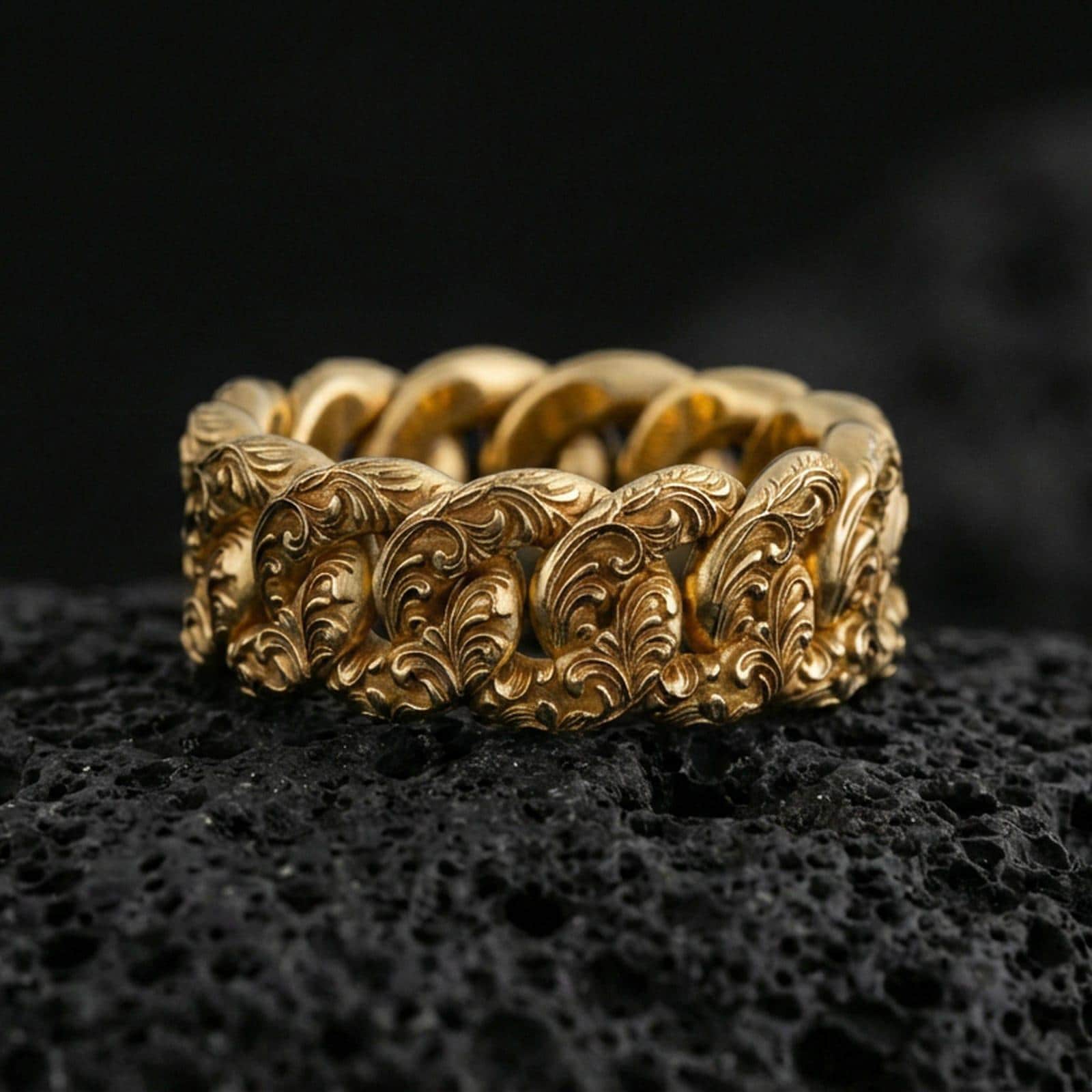 Gold plated Cuban link chain ring on volcanic rock, detailed interlocking links with engraved pattern, luxury jewelry product photography.