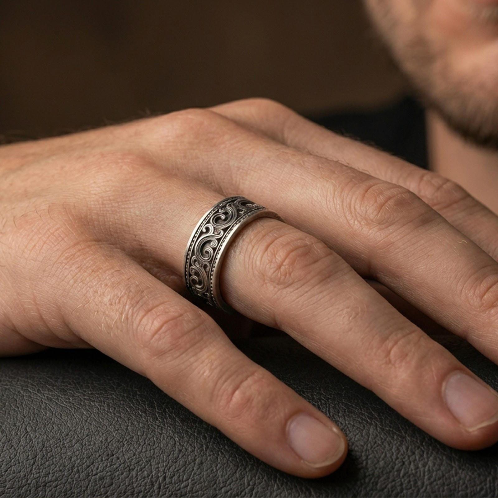 Oxidized sterling silver scrollwork band worn on finger, ornate swirl engraving and beaded edge detail, natural lifestyle hand shot with shallow depth of field.