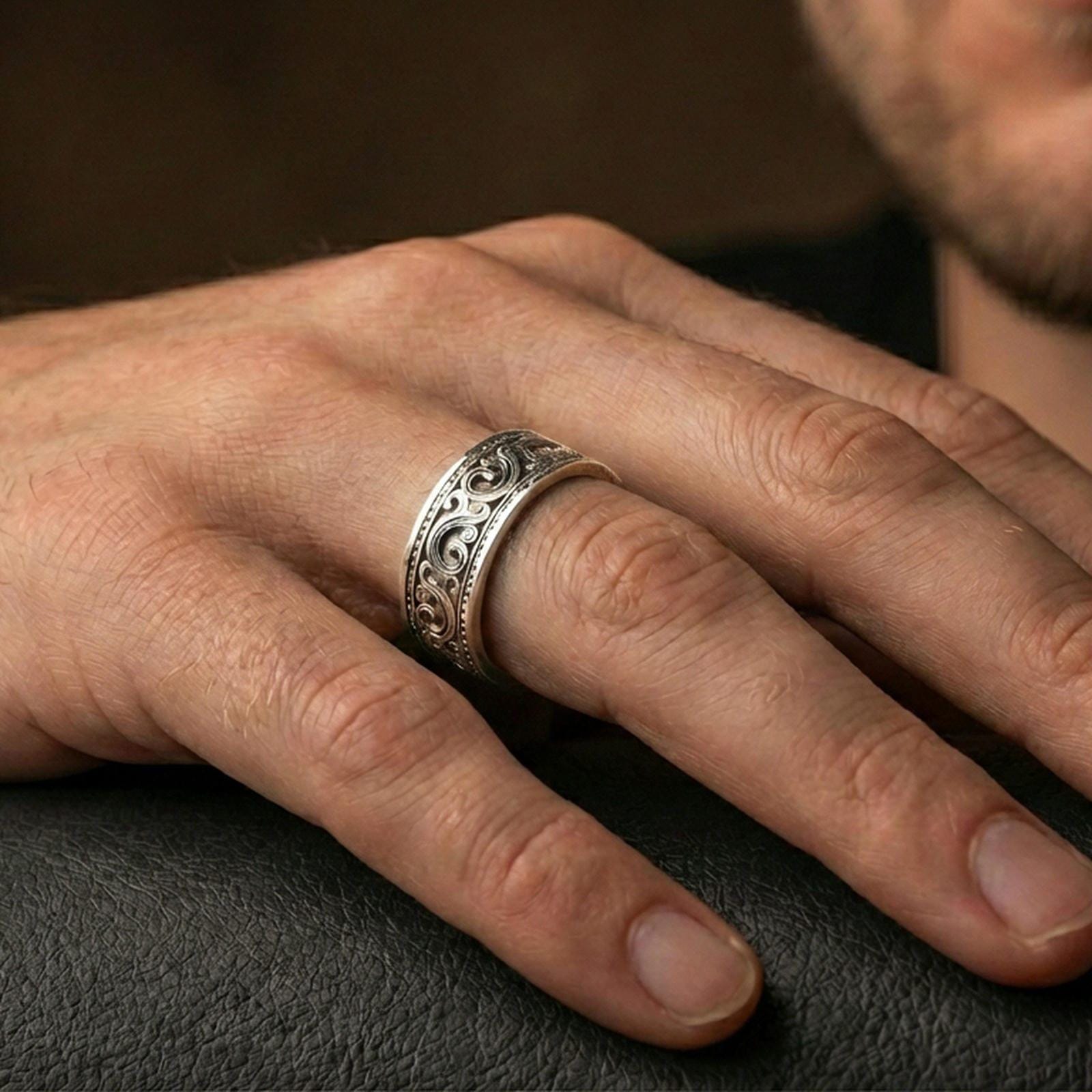 Polished silver engraved scroll band ring on finger, crisp filigree swirl detail with dotted borders, refined everyday wear close-up.