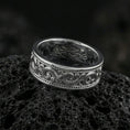 Load image into Gallery viewer, Polished silver engraved scroll band ring on black volcanic stone, crisp swirling filigree detail and dotted edge accents, centered close-up studio lighting.

