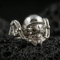 Load image into Gallery viewer, Polished silver gothic biker skull statement ring on black volcanic stone, crisp helmeted skull and mechanical frame details, centered close-up studio lighting.
