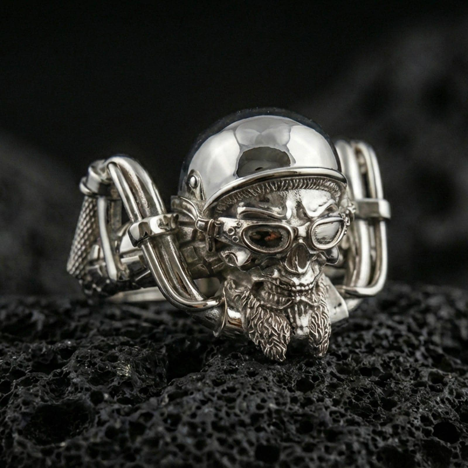 Polished silver gothic biker skull statement ring on black volcanic stone, crisp helmeted skull and mechanical frame details, centered close-up studio lighting.