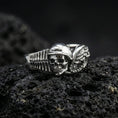 Load image into Gallery viewer, Polished silver gothic biker skull statement ring on black volcanic stone, crisp helmet skull with mechanical wing accents, centered close-up studio lighting.

