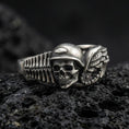 Load image into Gallery viewer, Oxidized sterling silver biker skull ring on dark volcanic rock, helmeted skull relief with wing and engine detail, premium macro product shot.

