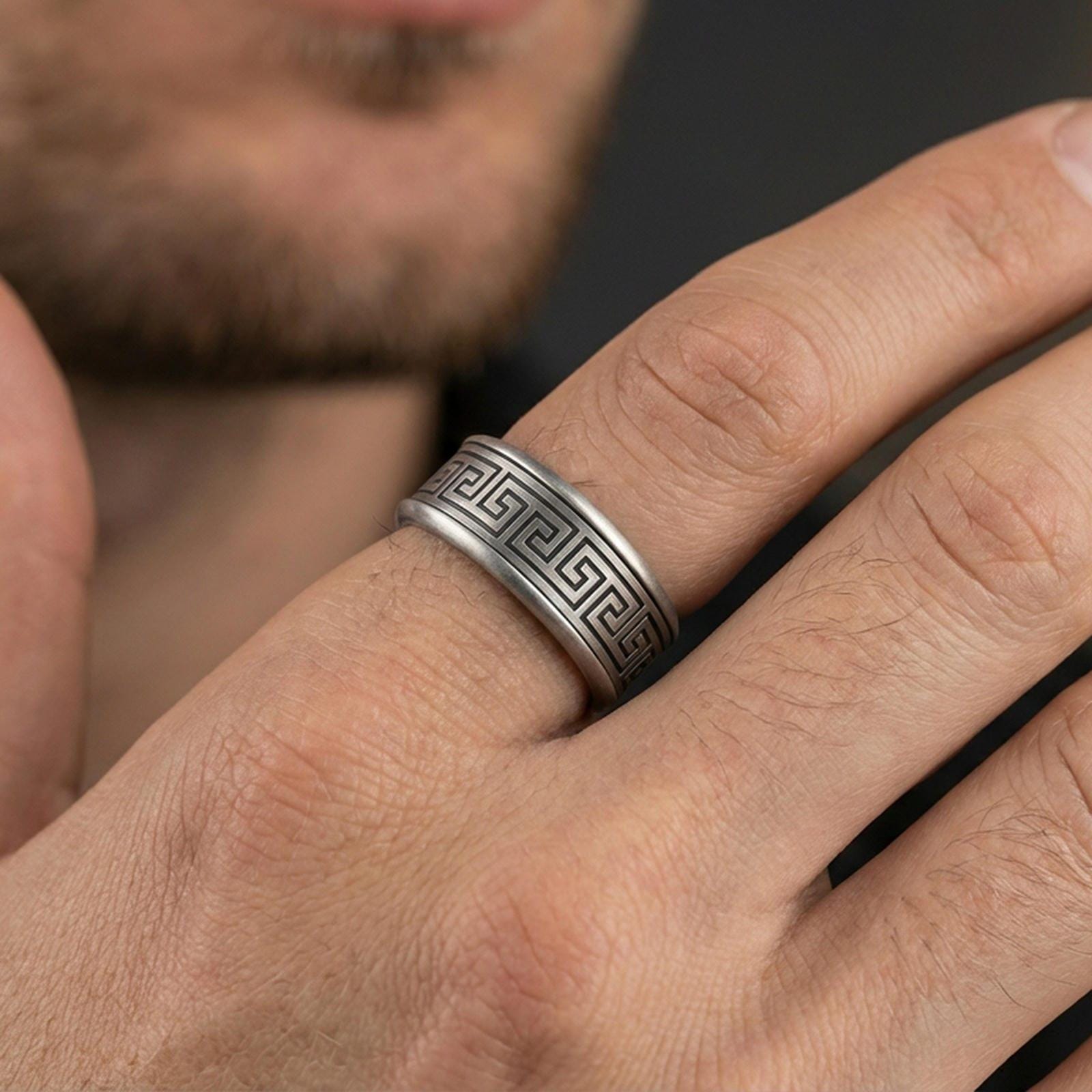 Oxidized sterling silver Greek key band worn on finger, meander pattern detail, natural lifestyle hand shot with shallow depth of field.
