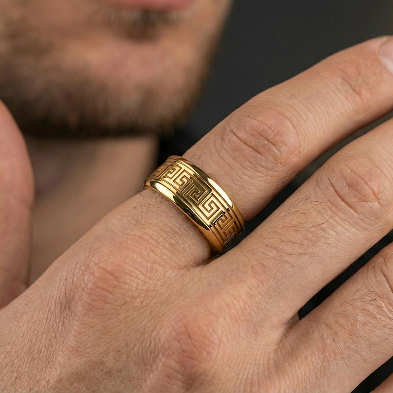 Gold plated Greek key pattern band worn on finger, classic meander motif detail, premium lifestyle jewelry photo.