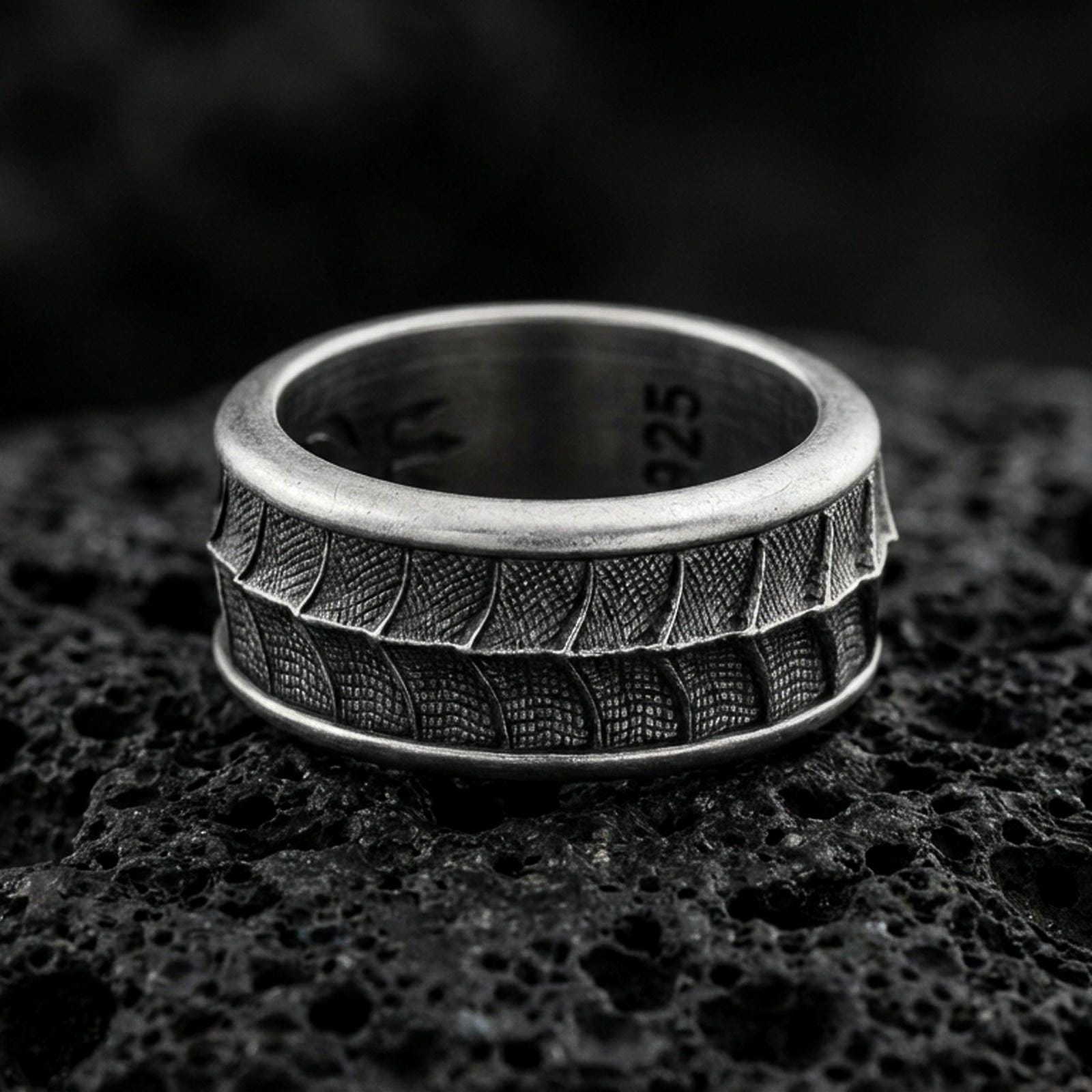 Oxidized sterling silver lizard scale spinner band ring on dark volcanic rock, textured reptile pattern on rotating center, premium macro product shot.