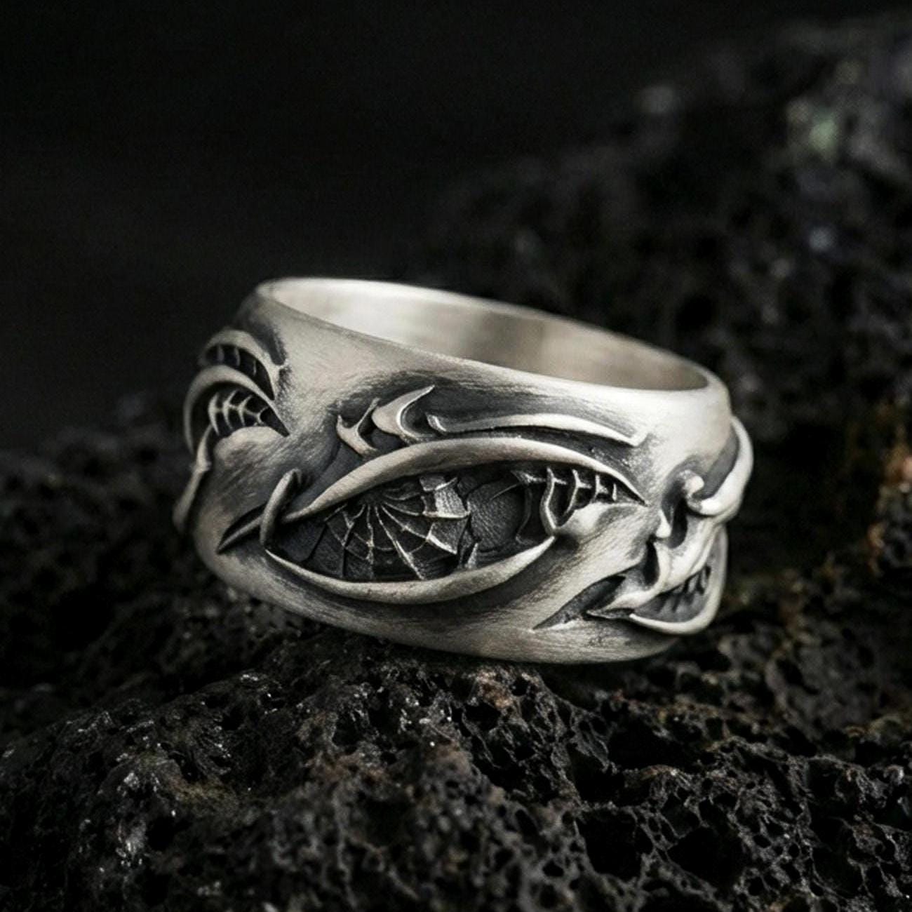 Oxidized sterling silver roots band ring on dark volcanic rock, organic vine and bark texture engraving, premium macro product shot.
