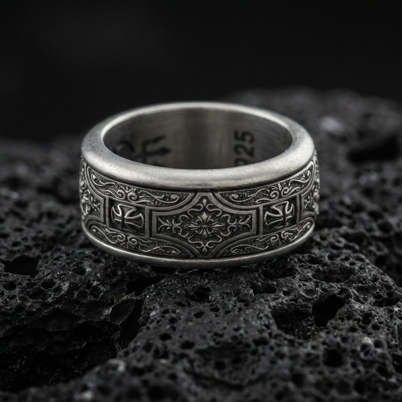 Oxidized sterling silver ornate filigree band ring on dark volcanic rock, vintage floral centerpiece and scroll engraving, premium macro product shot.