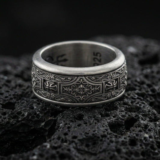 Oxidized sterling silver ornate filigree band ring on dark volcanic rock, vintage floral centerpiece and scroll engraving, premium macro product shot.