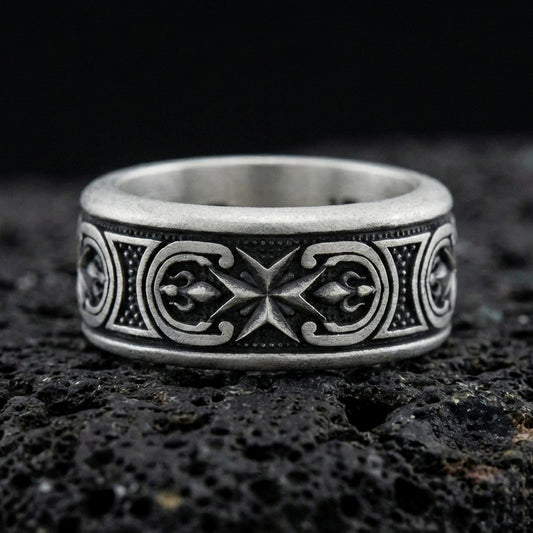 Oxidized sterling silver Maltese cross spinner band ring on dark volcanic rock, raised cross motif on rotating center with ornate side panels, premium macro product shot.