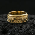 Load image into Gallery viewer, Gold plated bear scene band ring on volcanic rock, detailed bear engraving with rugged nature texture and knotwork accents, luxury jewelry product photography.
