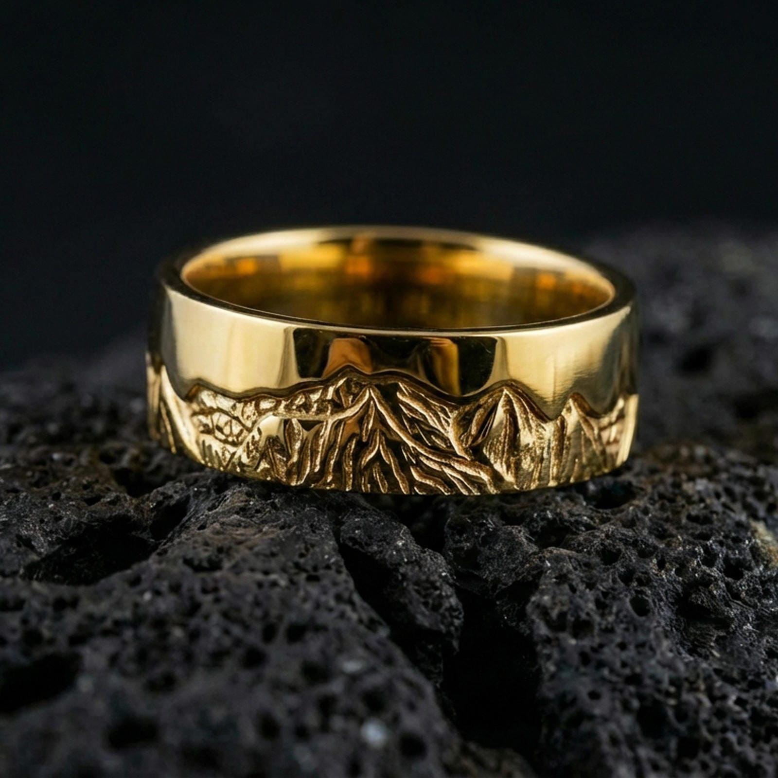 Gold plated Grand Teton mountain band ring on volcanic rock, detailed peak landscape engraving with rugged texture, luxury jewelry product photography.