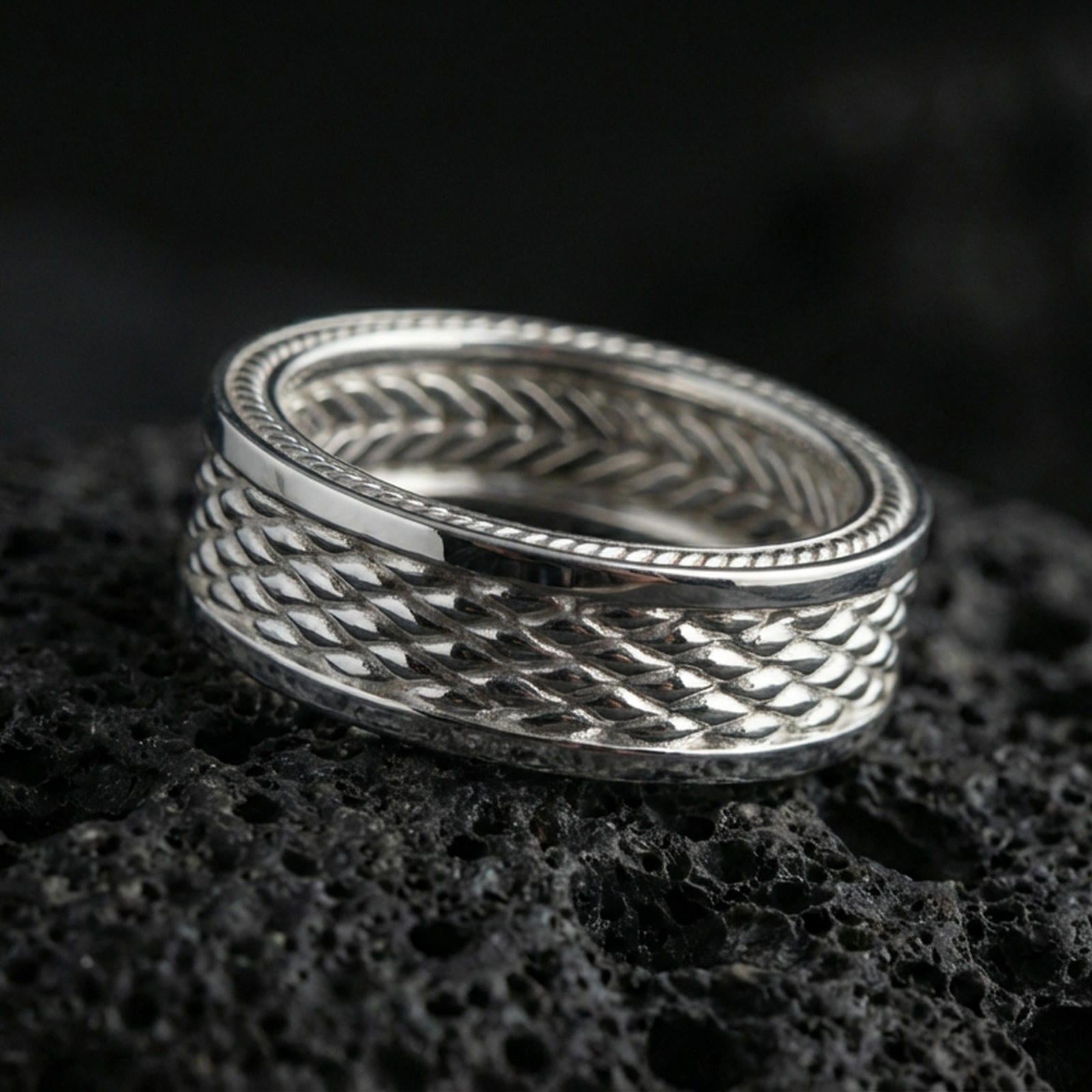 Polished silver braided rope band ring on black volcanic stone, crisp woven texture with beaded border accents, centered close-up studio lighting.