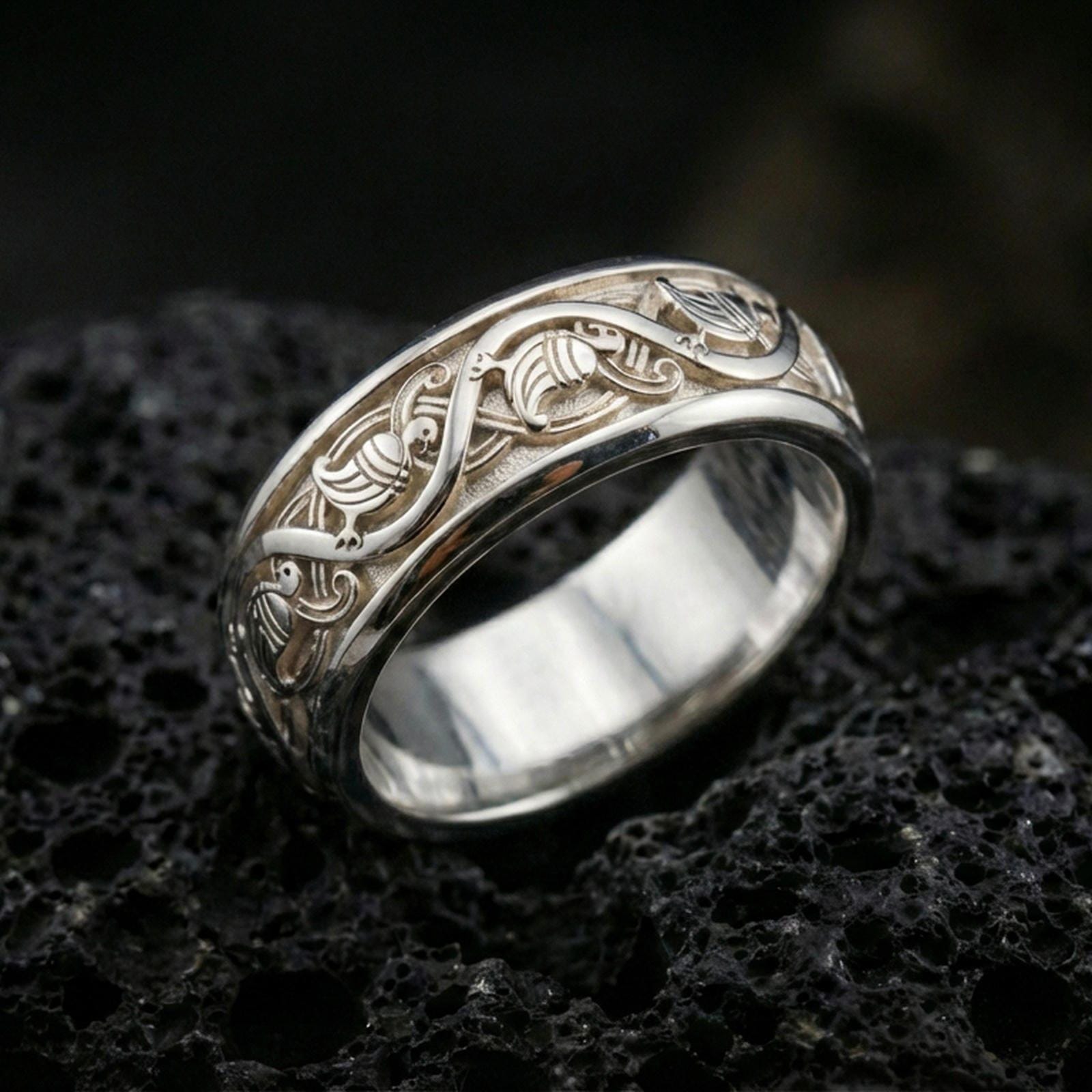 Polished silver dove engraved band ring on black volcanic stone, crisp pigeon motif and flowing vine details, centered close-up studio lighting.