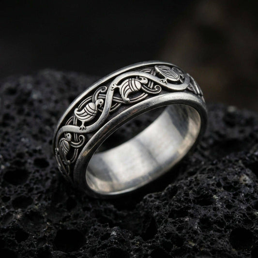Oxidized sterling silver dove pattern band ring on dark volcanic rock, repeating bird motif with elegant scrollwork, premium macro product shot.