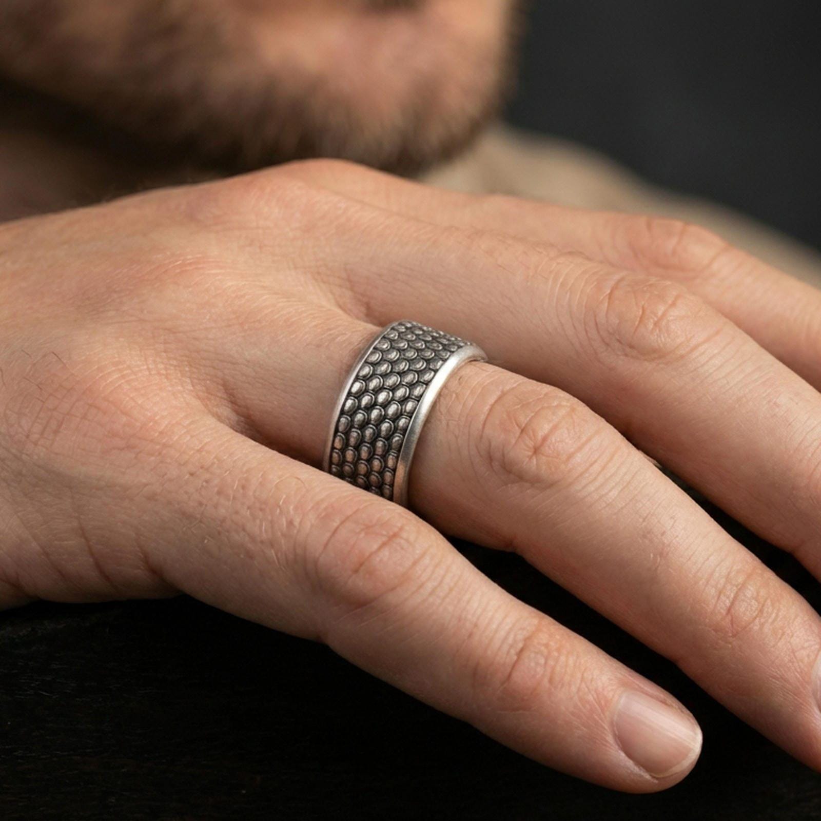 Oxidized sterling silver scale texture band worn on finger, repeating scale pattern detail, natural lifestyle hand shot with shallow depth of field.