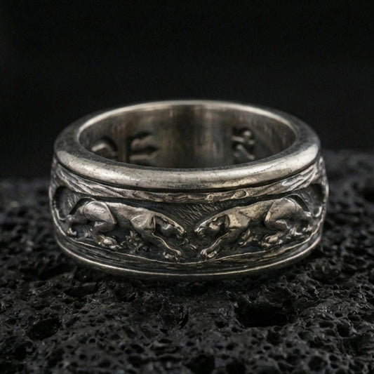 Oxidized sterling silver jaguar spinner band ring on dark volcanic rock, engraved big cat relief on rotating center with textured background, premium macro product shot.