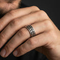 Load image into Gallery viewer, Oxidized sterling silver arrowhead spinner band worn on finger, tribal arrow pattern detail on rotating center, natural lifestyle hand shot with shallow depth of field.
