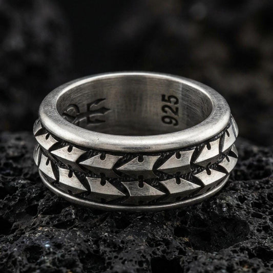 Oxidized sterling silver arrowhead spinner band ring on dark volcanic rock, tribal geometric chevron pattern on rotating center, premium macro product shot.