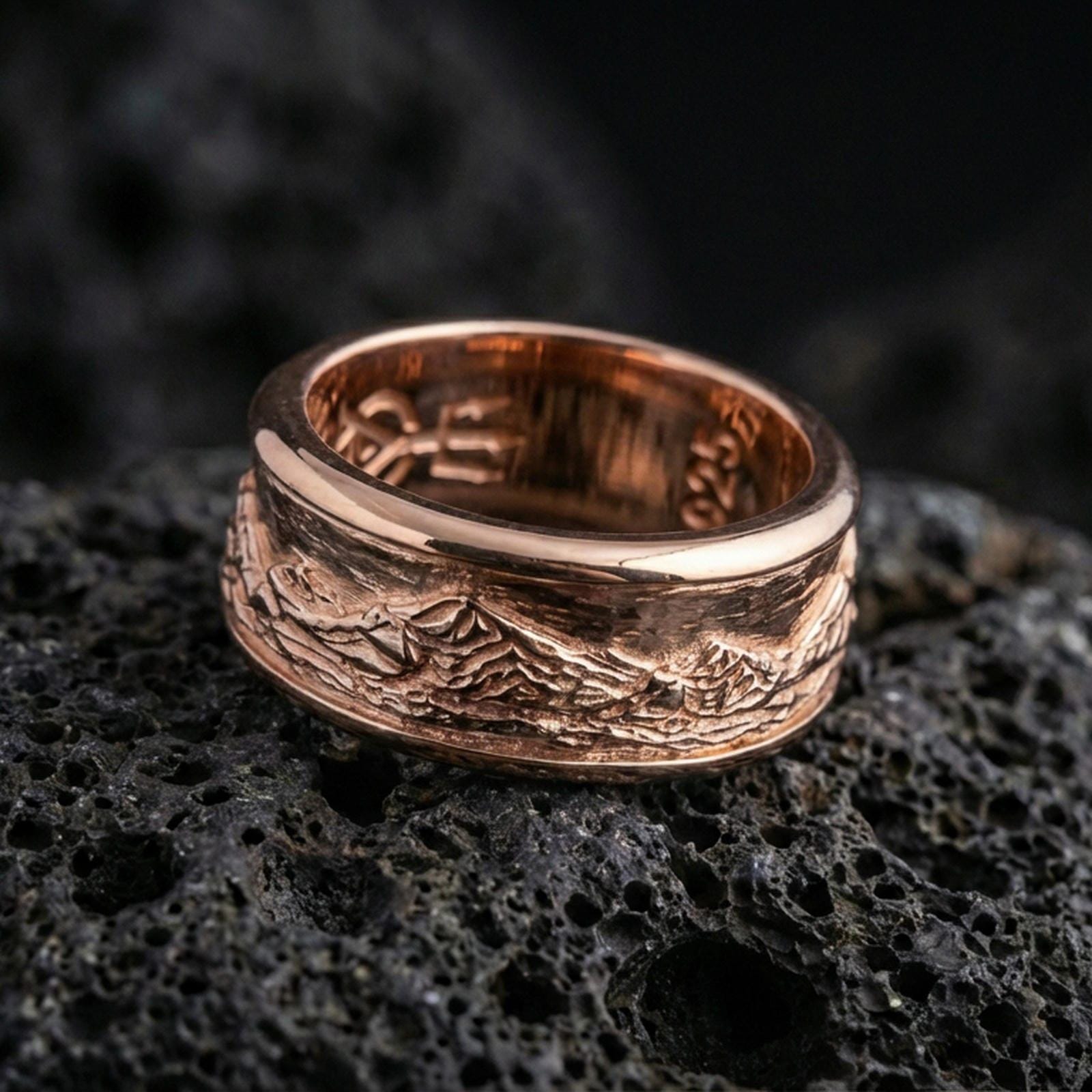 Rose gold plated sterling silver mountain landscape band on volcanic stone, engraved peak skyline with strong contrast detail, minimal high-end close-up.