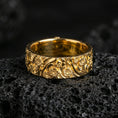Load image into Gallery viewer, Gold plated floral garden band ring on volcanic rock, detailed daisy blossoms with ornate leaf scrollwork, luxury jewelry product photography.
