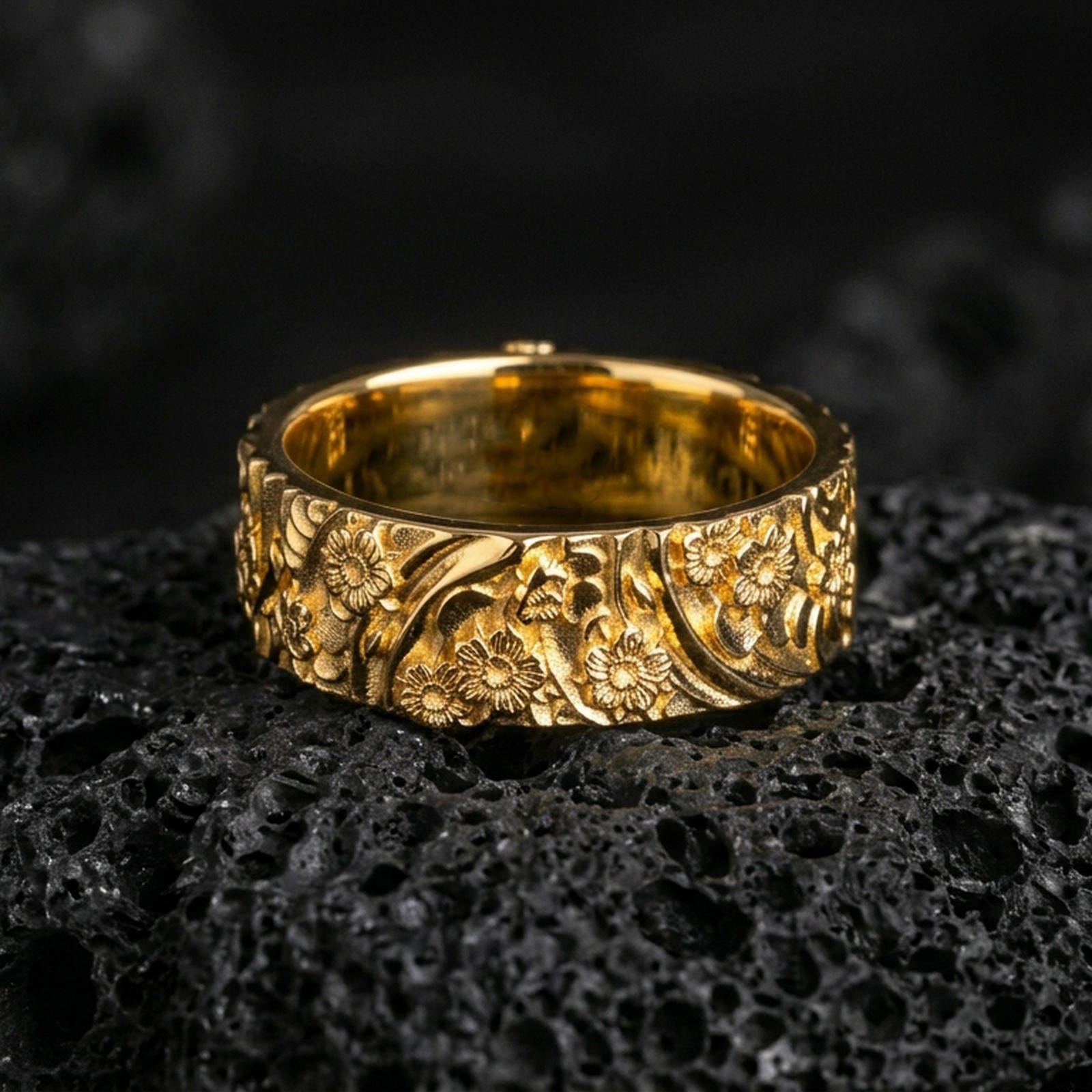 Gold plated floral garden band ring on volcanic rock, detailed daisy blossoms with ornate leaf scrollwork, luxury jewelry product photography.
