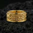 Load image into Gallery viewer, Gold plated jungle wildlife band ring on volcanic rock, detailed tropical foliage relief with animal engraving accents, luxury jewelry product photography.
