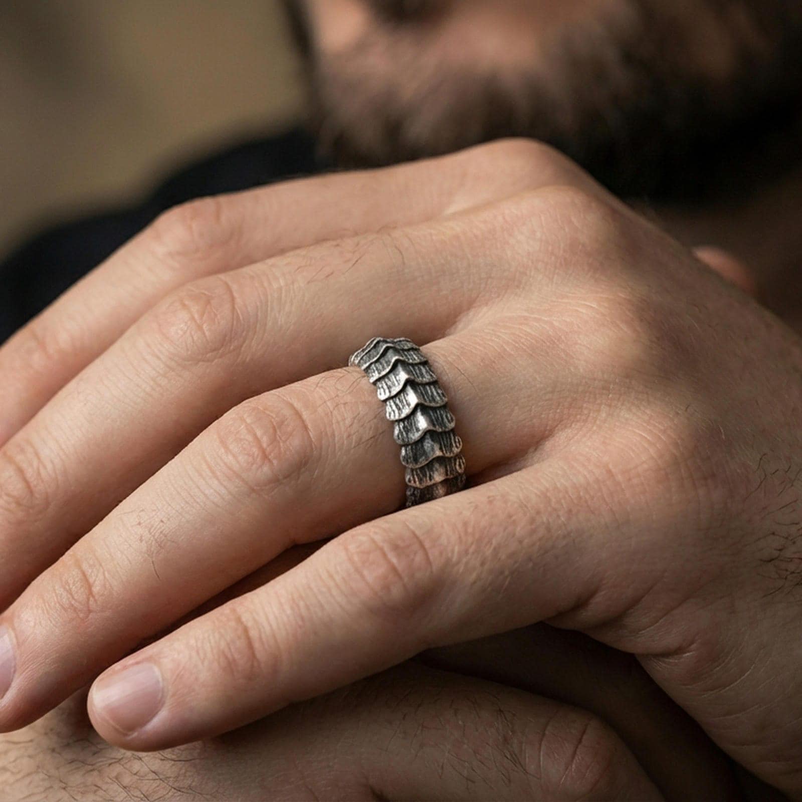 Oxidized sterling silver dragon scale band worn on finger, rugged segmented ridge texture detail, natural lifestyle hand shot with shallow depth of field.