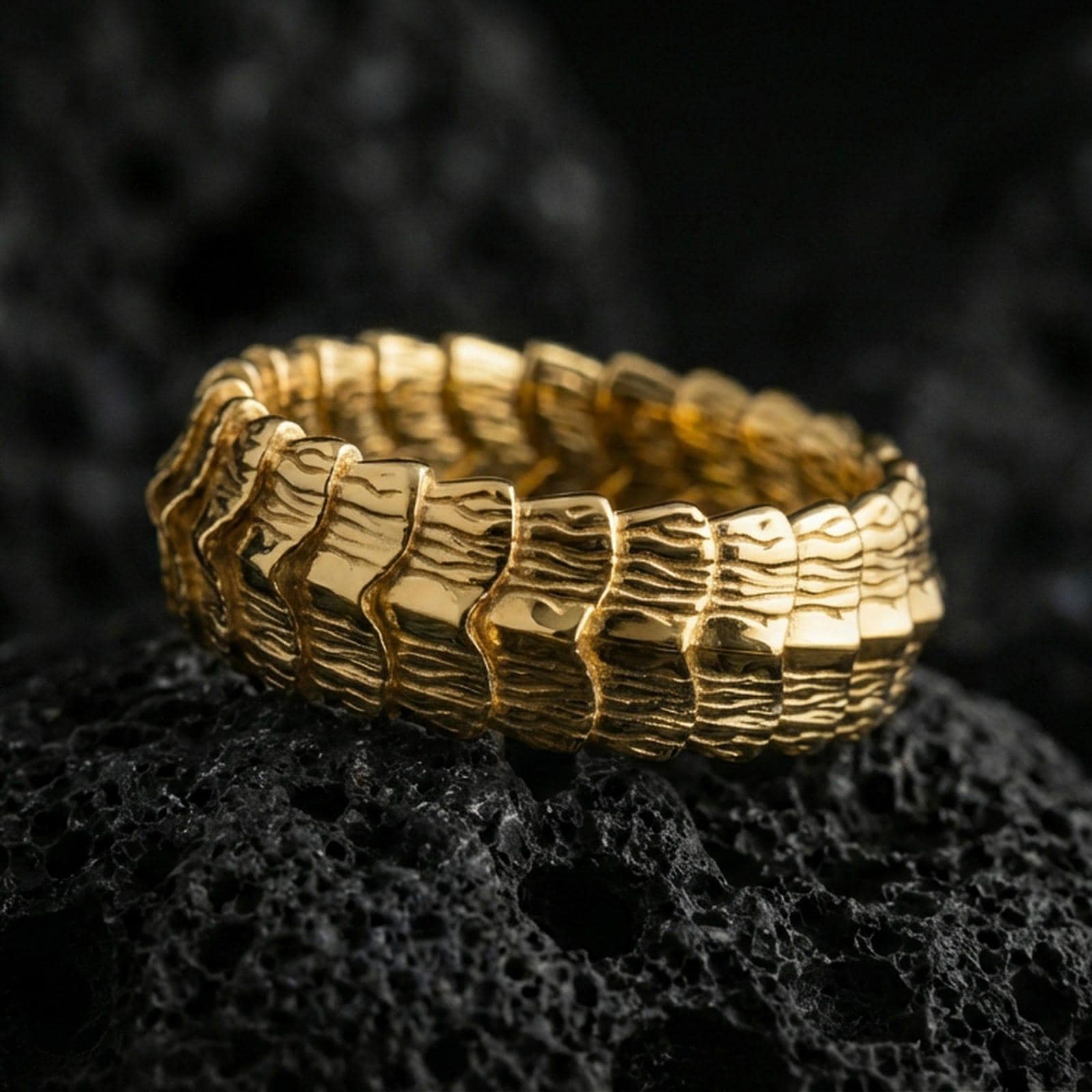 Gold plated dragon scale texture band ring on volcanic rock, detailed segmented ridge pattern with bold depth, luxury jewelry product photography.
