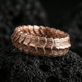 Load image into Gallery viewer, Rose gold plated sterling silver dragon scale band on volcanic stone, sculpted layered ridge texture with strong contrast, minimal high-end close-up.
