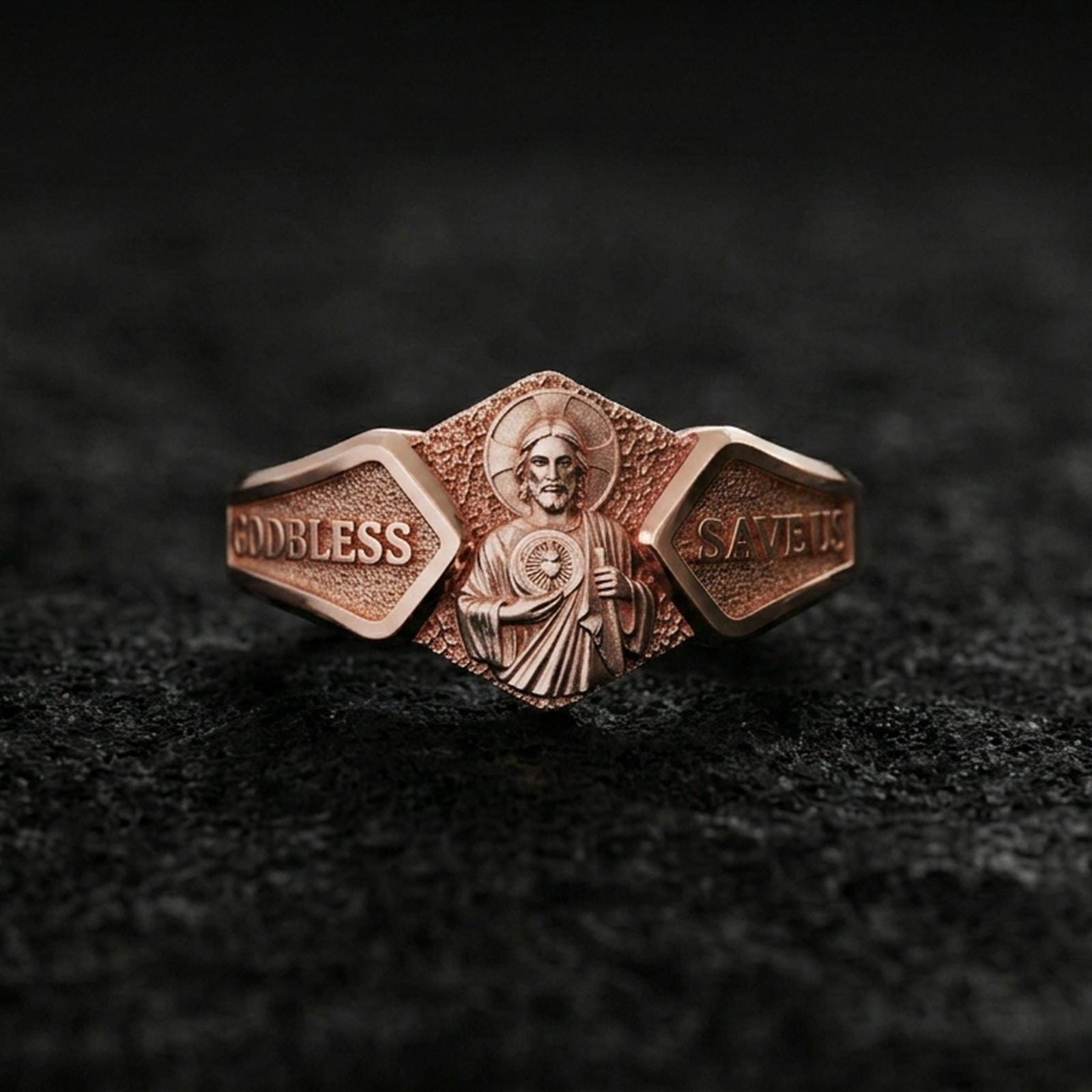 Rose gold plated sterling silver Saint Jude ring on volcanic stone, sculpted saint portrait relief with bold engraved text panels, minimal high-end close-up.