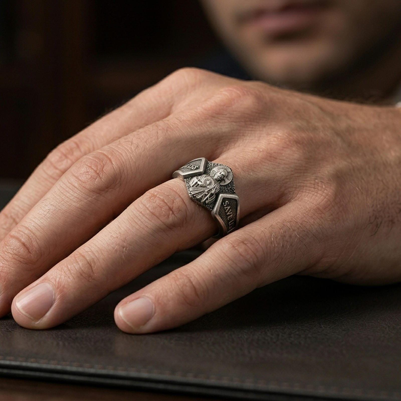 Oxidized sterling silver Saint Jude signet ring worn on finger, saint portrait relief with “God Bless” and “Save Us” engraving, natural lifestyle hand shot with shallow depth of field.