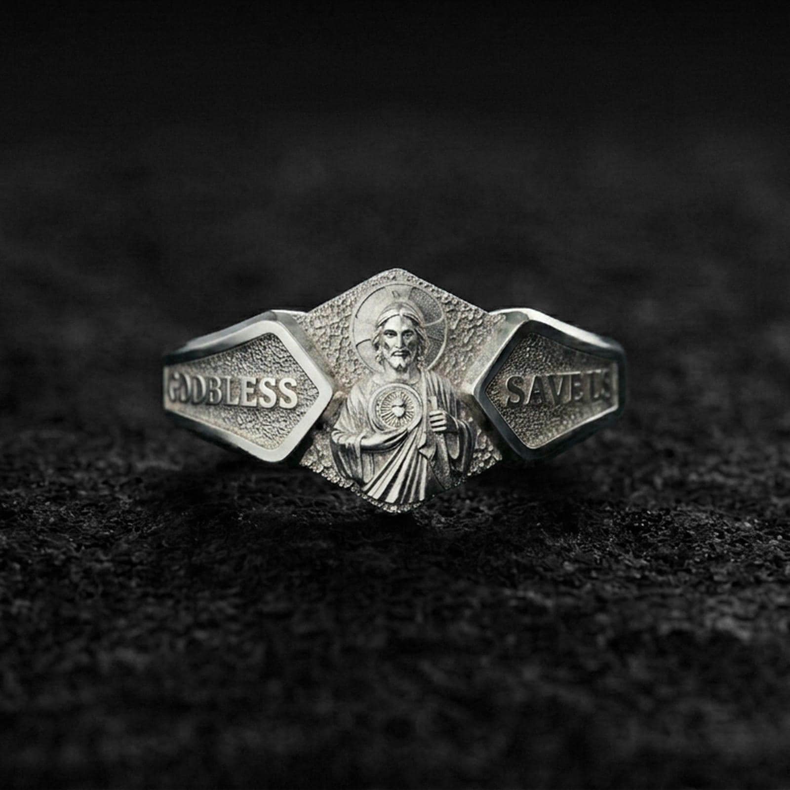 Polished silver Saint Jude religious signet ring on black volcanic stone, crisp saint portrait relief with engraved “God Bless” and “Save Us” text, centered close-up studio lighting.