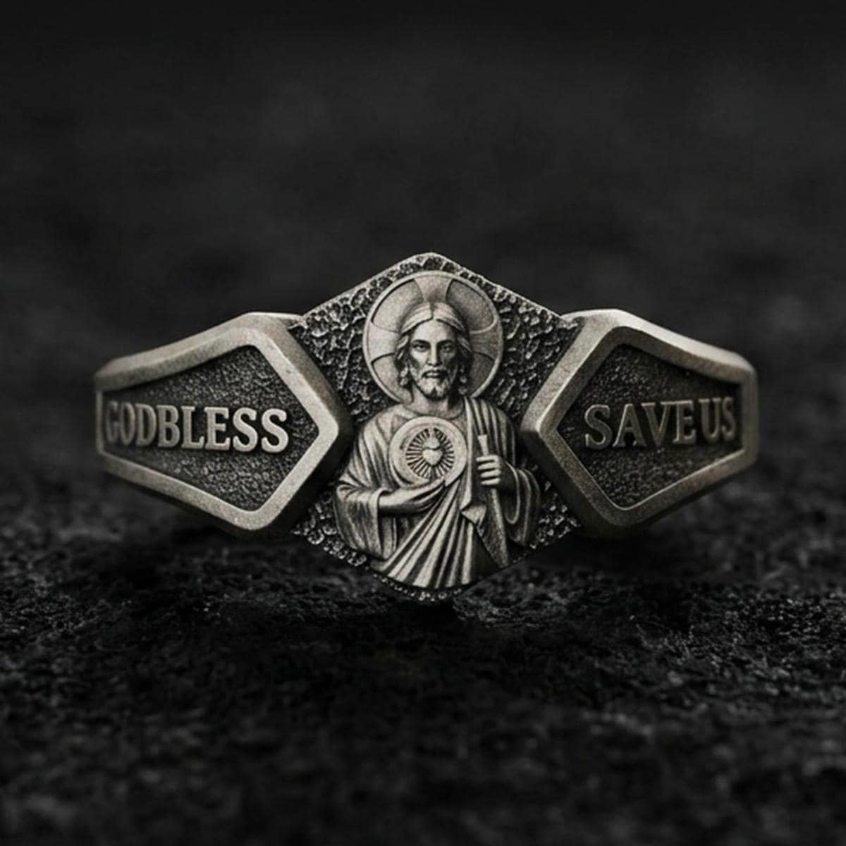 Oxidized sterling silver Saint Jude signet ring on dark volcanic rock, detailed halo portrait relief with “God Bless” and “Save Us” panels, premium macro product shot.