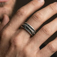 Load image into Gallery viewer, Oxidized sterling silver arrow spinner band worn on finger, arrow motif detail on rotating center, natural lifestyle hand shot with shallow depth of field.
