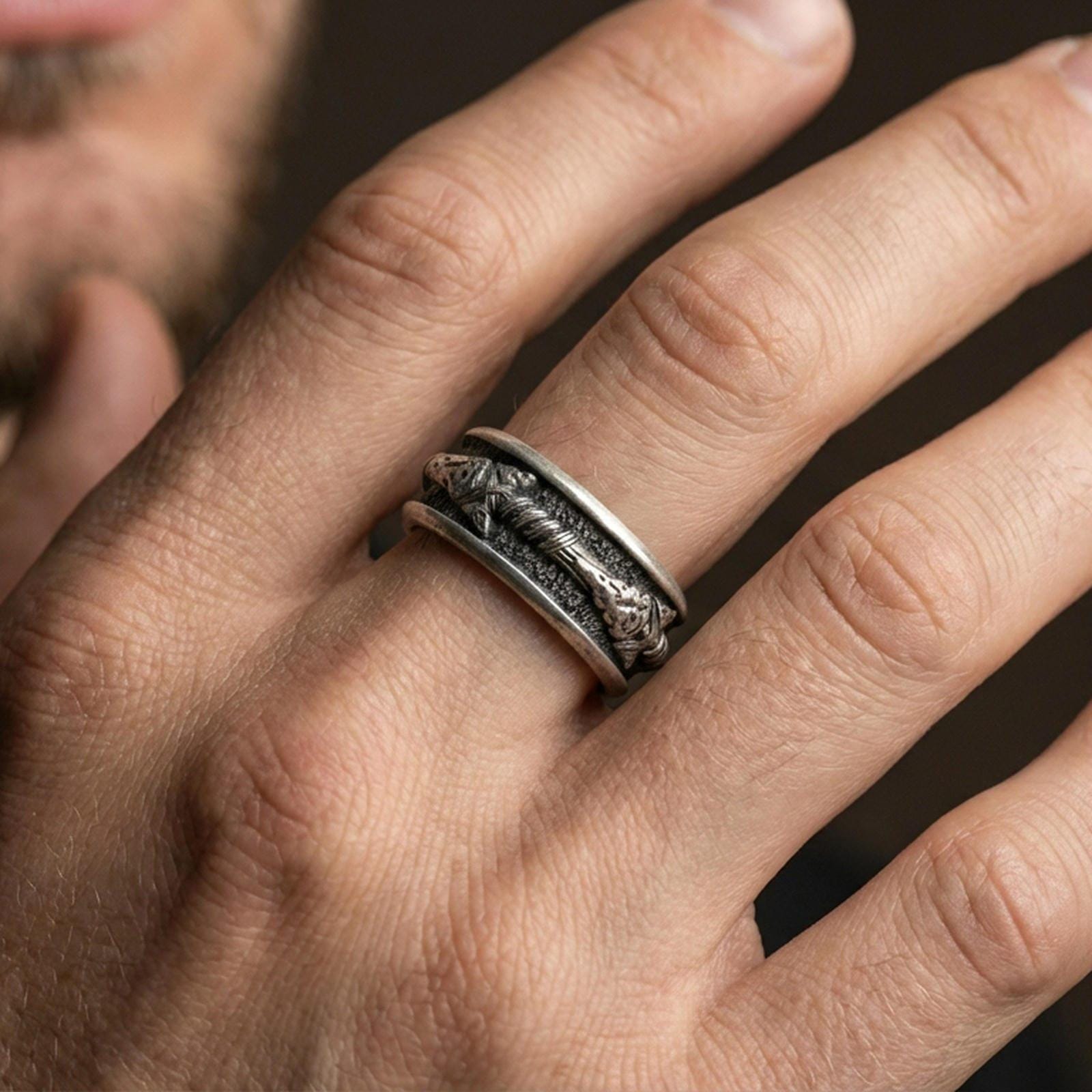 Oxidized sterling silver arrow spinner band worn on finger, arrow motif detail on rotating center, natural lifestyle hand shot with shallow depth of field.