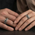 Load image into Gallery viewer, Oxidized sterling silver skull and koi spinner band worn on finger, skull relief with carp and wave detail on rotating center, natural lifestyle hand shot with shallow depth of field.
