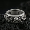 Load image into Gallery viewer, Oxidized sterling silver skull and koi spinner band ring on dark volcanic rock, detailed skull relief with carp, clouds, and wave motifs on rotating center, premium macro product shot.
