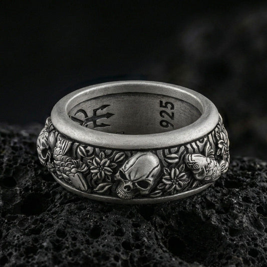 Oxidized sterling silver skull and koi spinner band ring on dark volcanic rock, detailed skull relief with carp, clouds, and wave motifs on rotating center, premium macro product shot.