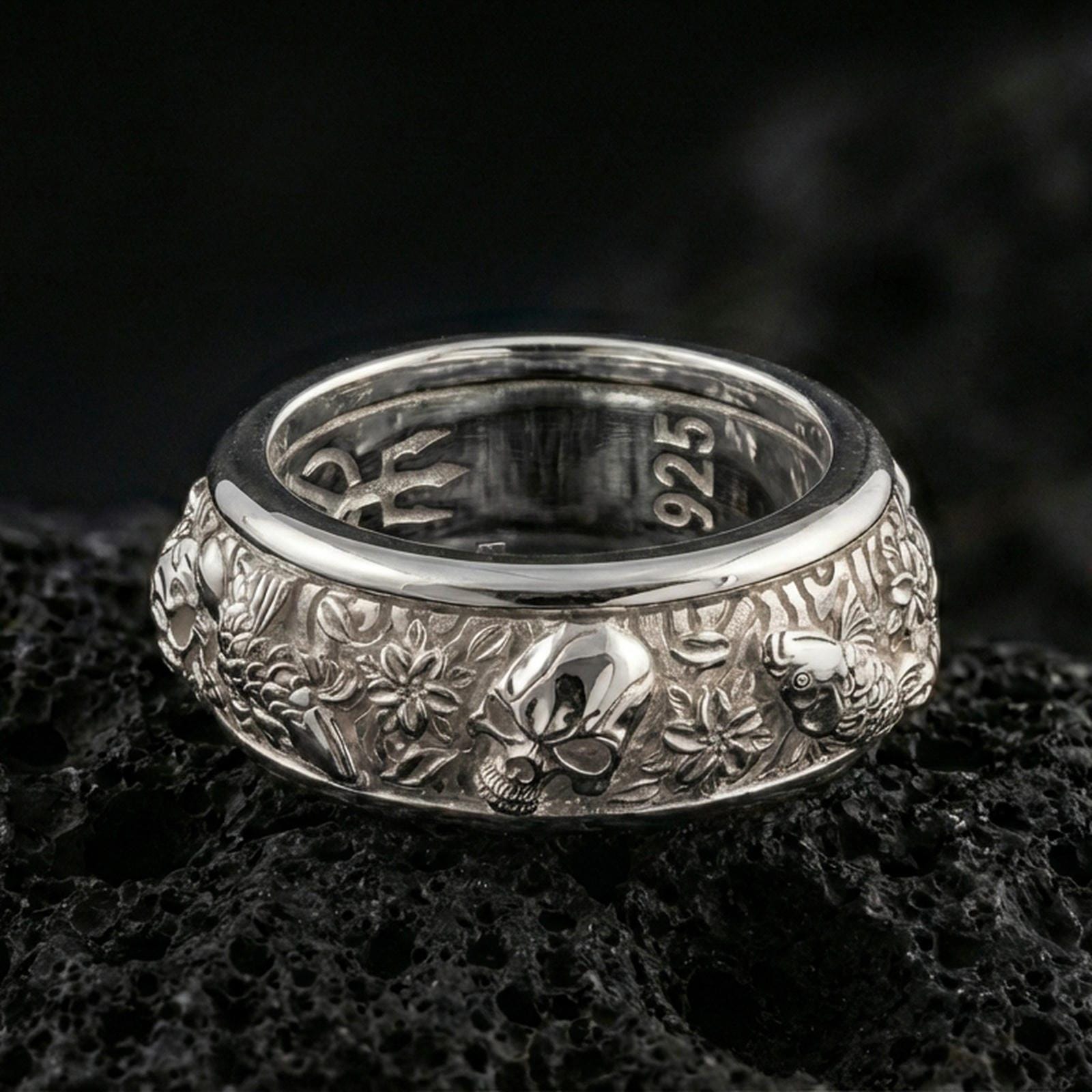 Polished silver skull and koi fidget spinner ring on black volcanic stone, crisp skull relief with carp and floral wave texture, centered close-up studio lighting.