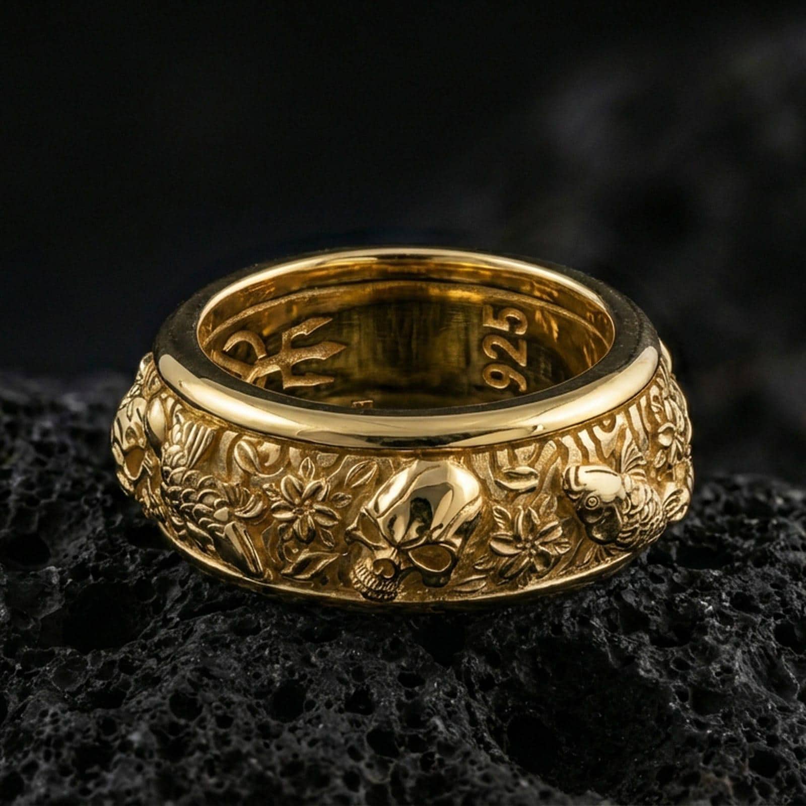 Gold plated skull and koi spinner band ring on volcanic rock, detailed skull relief with carp, clouds, and wave pattern on rotating band, luxury jewelry product photography.