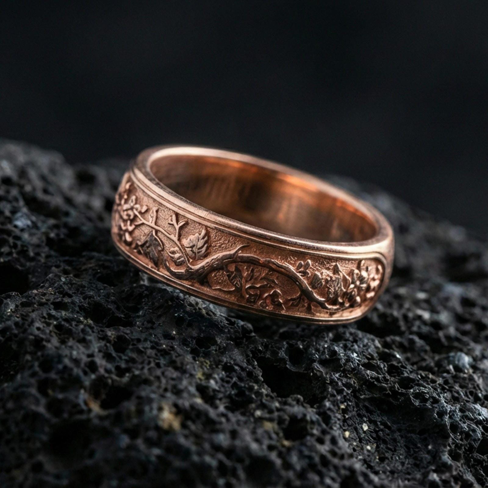 Rose gold plated sterling silver tree branch band on volcanic stone, sculpted root and leaf relief with deep contrast, minimal high-end close-up.